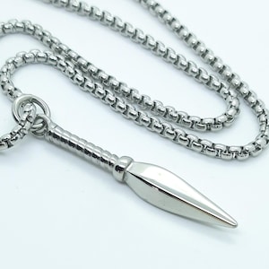 May include: A silver necklace featuring a spearhead pendant. The chain is composed of small, linked segments. The pendant has a polished, elongated form with a sharp point. The necklace is set against a white backdrop.