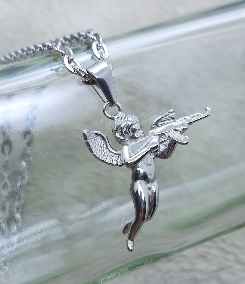 Pu&ograve; includere: Collana con catena d'argento con un ciondolo a forma di cherubino che tiene una pistola. Il cherubino ha le ali ed &egrave; in una posa di volo.