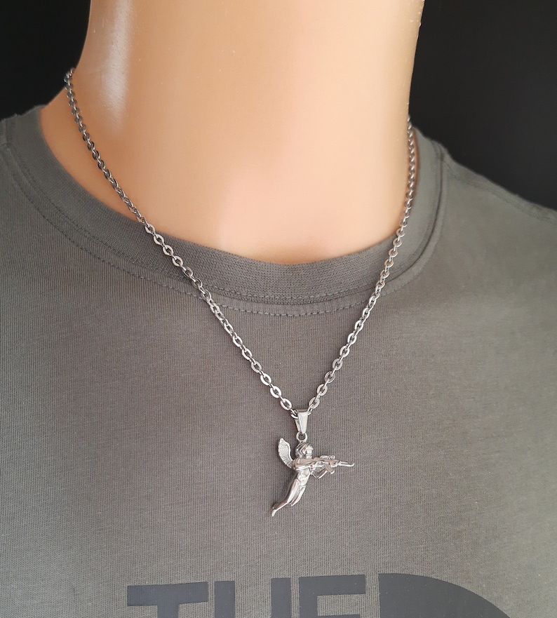 Pu&ograve; includere: Una collana a catena d'argento con un ciondolo a forma di angelo d'argento che tiene una pistola. L'angelo sta volando con le ali spiegate.