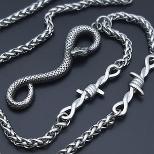 May include: A silver-toned metal necklace featuring a textured snake pendant coiled into a loop. The chain is composed of interlocking links and incorporates two distinct segments designed to resemble twisted wire with sharp, protruding barbs.