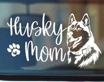 May include: White decal featuring the words "Husky Mom" in a script font, with a paw print and heart symbol. A detailed illustration of a Husky dog is on the right. The design is suitable for car windows or other surfaces.