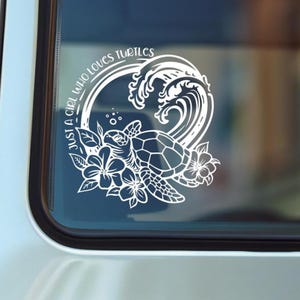 May include: A white vinyl decal applied to a window featuring a sea turtle surrounded by tropical flowers and a large ocean wave. The text "JUST A GIRL WHO LOVES TURTLES" is arched along the left side of the circular graphic design.