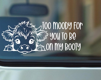 May include: A white vinyl decal featuring a stylized illustration of a fluffy Highland cow peering over a ledge, accompanied by the text "TOO MOODY FOR YOU TO BE ON MY BOOTY" in a playful, rounded sans-serif font, designed for application on glass.