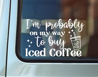 May include: White vinyl decal on a car window. The decal reads "I'm probably on my way to buy Iced Coffee" with a graphic of an iced coffee drink. The decal is designed to be applied to a car window.