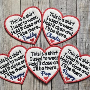 May include: Heart-shaped patches with red trim and embroidered text. Each patch has the phrase "This is a shirt I used to wear, Hold it close and I'll be there." with names like "Daddy" and "Charlie" in blue.