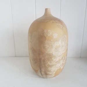 Op de afbeelding: Een beige keramische vaas met een bloemenmotief. De vaas heeft een rond lichaam en een smalle hals.