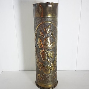 Può includere: Un vaso in ottone con un motivo floreale in rilievo sul lato. Il vaso è realizzato da un proiettile di artiglieria riutilizzato.