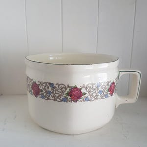 Könnte beinhalten: Cremefarbene Keramikschale mit Henkel und einem dekorativen Blumenband mit roten Rosen und blauen Akzenten. Der Rand und der Henkel sind grün umrandet. Ein Stück im Vintage-Stil.