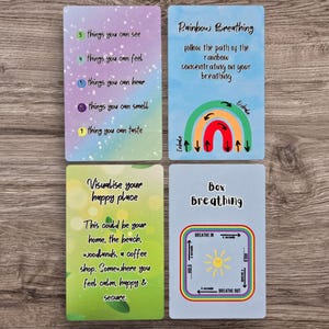May include: Four cards with mindfulness prompts. One card lists senses, another guides "Rainbow Breathing," a third encourages visualizing a happy place, and the last illustrates "Box Breathing." The cards have colorful designs and text.