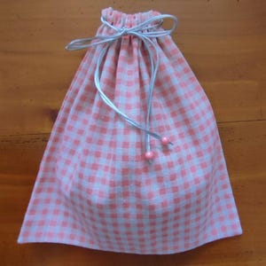 Pode incluir: Uma bolsa de cordão de vichy rosa e branco com uma fita cinza e contas cor-de-rosa.