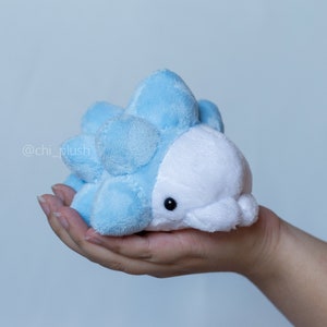 May include: A blue and white plush toy resembling a spiky, round creature. The toy has a white face with black eyes and a small mouth.