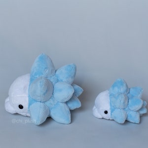 Puede incluir: Dos peluches de un personaje Pok&eacute;mon azul y blanco, uno m&aacute;s grande que el otro. El peluche m&aacute;s grande est&aacute; tumbado de lado, mientras que el m&aacute;s peque&ntilde;o est&aacute; de pie. Ambos peluches tienen una concha azul puntiaguda y un cuerpo blanco.