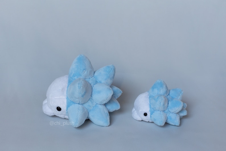 Puede incluir: Dos peluches de un personaje Pok&eacute;mon azul y blanco, uno m&aacute;s grande que el otro. El peluche m&aacute;s grande est&aacute; tumbado de lado, mientras que el m&aacute;s peque&ntilde;o est&aacute; de pie. Ambos peluches tienen una concha azul puntiaguda y un cuerpo blanco.