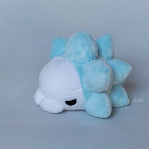 Puede incluir: Un juguete de peluche que se asemeja a un personaje Pok&eacute;mon azul y blanco. El juguete tiene una cara blanca con ojos negros y un cuerpo azul puntiagudo.