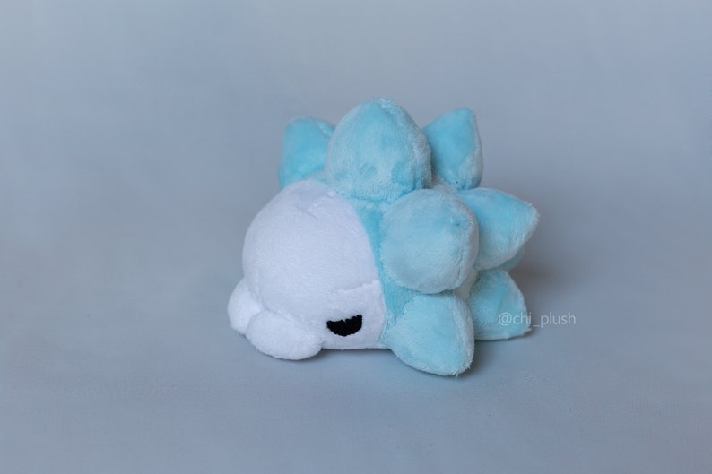 Puede incluir: Un juguete de peluche que se asemeja a un personaje Pok&eacute;mon azul y blanco. El juguete tiene una cara blanca con ojos negros y un cuerpo azul puntiagudo.