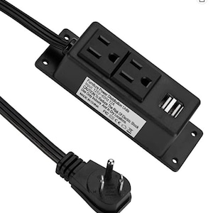 May include: Black power strip with two standard electrical outlets and two USB ports. The power strip has a black cord with a three-prong plug. The text on the power strip reads: "Furniture Power Distribution Units Input: 125V-60Hz 12A CAUTION: To Reduce The Risk Of Electric Shock Use Only Indoors And in Dry Locations. MADE IN CHINA  CE"