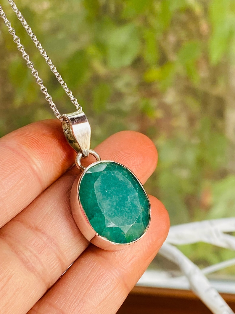 May include: A silver chain necklace with a pendant featuring a large, oval-shaped emerald green gemstone.