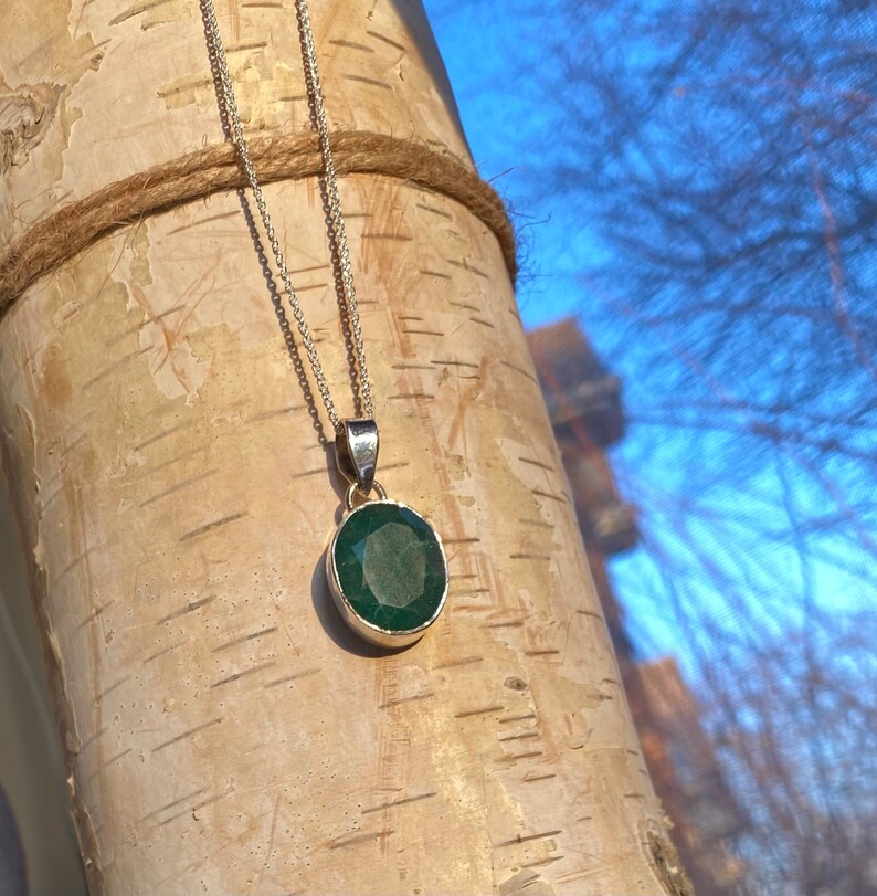 May include: A silver chain necklace with a dark green gemstone pendant. The pendant is round and has a faceted cut.