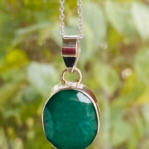 May include: A silver chain necklace with a pendant featuring a large, oval-shaped emerald green gemstone.