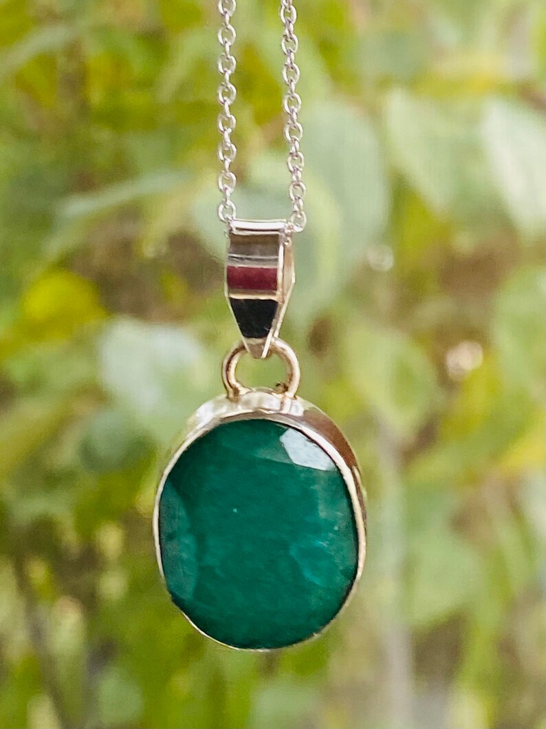 May include: A silver chain necklace with a pendant featuring a large, oval-shaped emerald green gemstone.