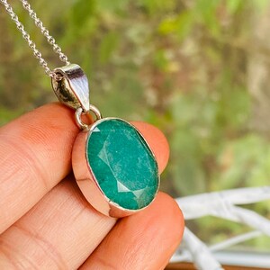 May include: A silver chain necklace with a pendant featuring a large, oval-shaped emerald green gemstone.