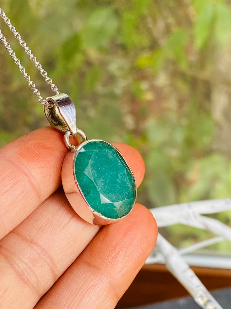 May include: A silver chain necklace with a pendant featuring a large, oval-shaped emerald green gemstone.
