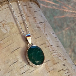May include: A silver chain necklace with a pendant featuring a large, oval-shaped, dark green gemstone.