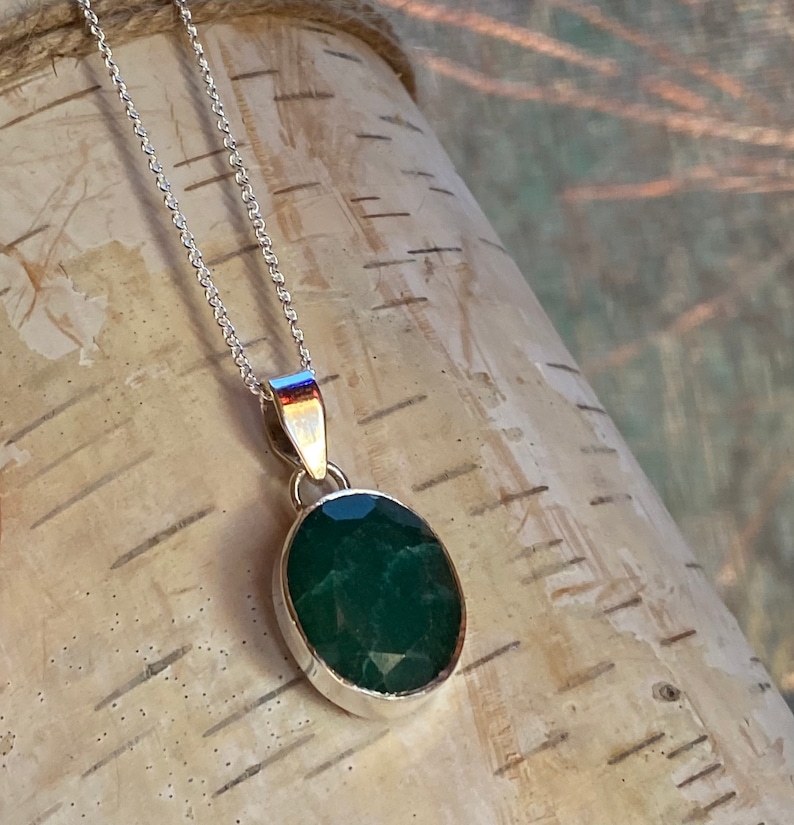May include: A silver chain necklace with a pendant featuring a large, oval-shaped, dark green gemstone.