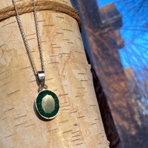 May include: A silver chain necklace with a pendant featuring a dark green oval gemstone.
