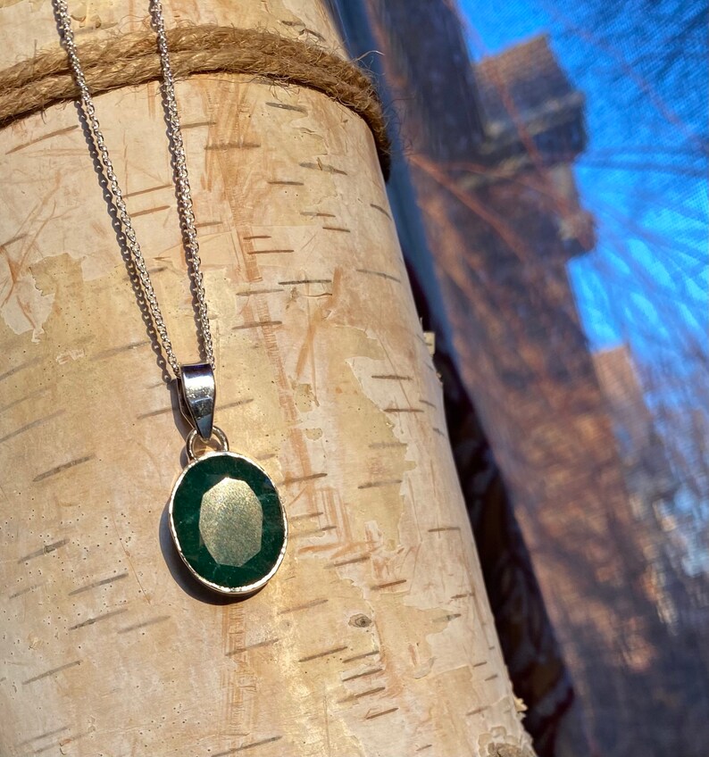 May include: A silver chain necklace with a pendant featuring a dark green oval gemstone.