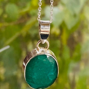 May include: A silver chain necklace with a pendant featuring a large, oval-shaped emerald gemstone.