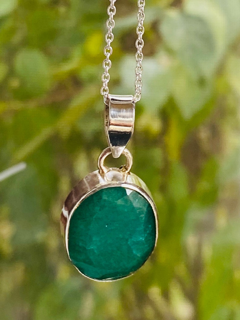 May include: A silver chain necklace with a pendant featuring a large, oval-shaped emerald gemstone.
