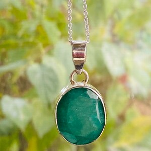 May include: A silver chain necklace with a pendant featuring a large, oval-shaped emerald gemstone.