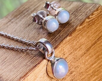 May include: A silver necklace and earrings set with a white pearl pendant and matching stud earrings.