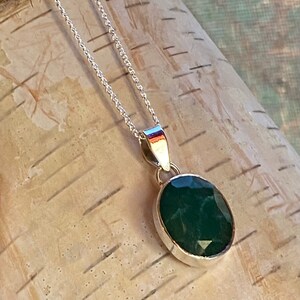May include: A silver chain necklace with a dark green oval pendant. The pendant is set in silver and has a faceted design.