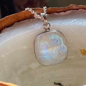 May include: A silver chain necklace with a white moonstone pendant. The moonstone is a rectangular shape with a pearlescent sheen.