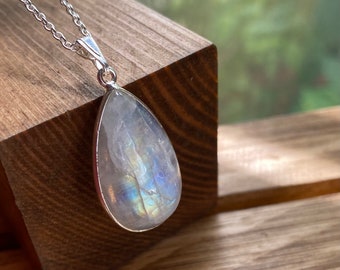 May include: A silver chain necklace with a teardrop-shaped moonstone pendant. The pendant has a rainbow iridescent sheen.