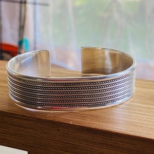 May include: A silver bangle bracelet with a textured design of rope-like lines.