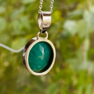 May include: A silver chain necklace with a green gemstone pendant. The pendant is round and has a smooth, polished surface.