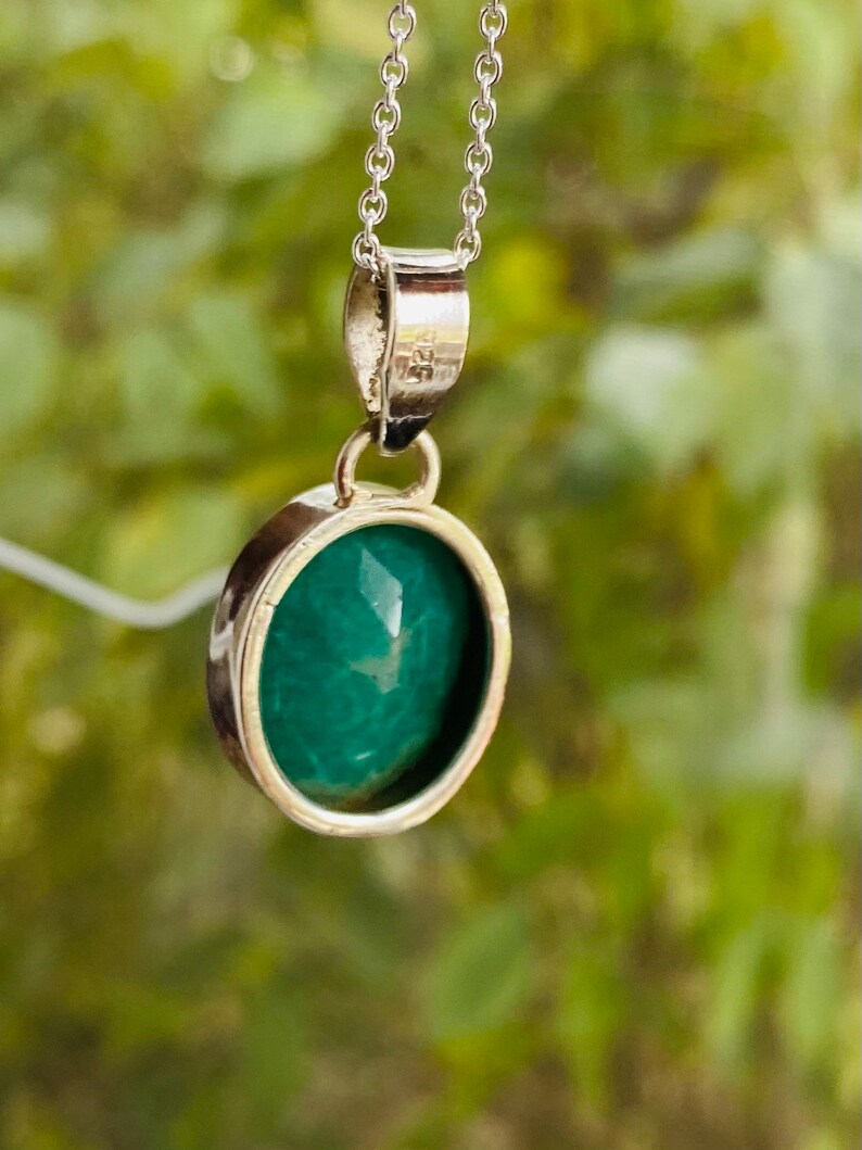 May include: A silver chain necklace with a green gemstone pendant. The pendant is round and has a smooth, polished surface.