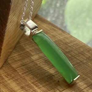 May include: A silver chain necklace with a green stone pendant. The pendant is a long, rectangular shape with rounded edges.