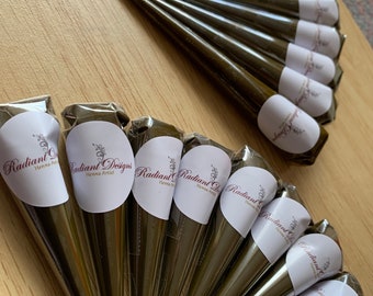 May include: A close-up of several brown henna cones with white labels that say "Radiant Designs Henna Artist".