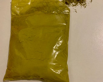 May include: A clear plastic bag filled with a green powder. Some of the powder has spilled out of the bag onto a white surface.