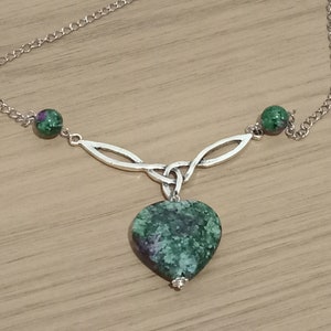 May include: A silver Celtic knot necklace with a green and pink heart-shaped pendant and two green and pink round beads.