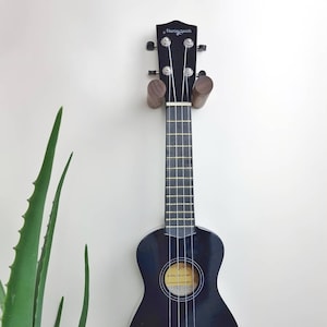 Może przedstawiać: Czarny ukulele z drewnianym uchwytem na ścianę. Ukulele ma logo Martin Smith na główce.
