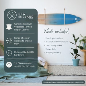 K&ouml;nnte beinhalten: Eine Surfboard-Wandhalterung aus Holz mit einem blauen und wei&szlig;en Farbverlauf. Sie enth&auml;lt zwei Lederriemen, Eichen-Verriegelungsd&uuml;bel, H&auml;ngebolzen und Maueranker. Die Halterung ist an einer wei&szlig;en Wand mit einer gr&uuml;nen Pflanze in einem blauen Topf befestigt.