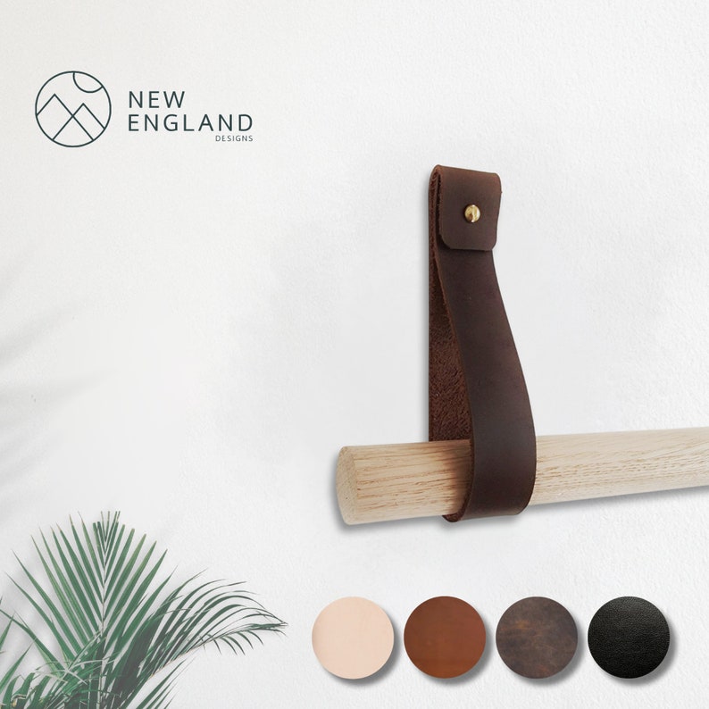 May include: A brown leather strap with a brass rivet is attached to a wooden dowel. The strap is used to hang a towel rack on a wall. The dowel is about 1 inch in diameter. The strap is about 1.5 inches wide. The strap is about 6 inches long. The strap is available in five colors: light brown, brown, dark brown, black, and gray.