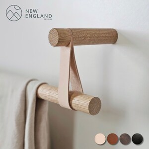 Puede incluir: Un toallero de madera con una correa de cuero. La barra est&aacute; montada en una pared blanca. El toallero est&aacute; hecho de madera natural y tiene un acabado marr&oacute;n claro. La correa de cuero es de color marr&oacute;n claro y est&aacute; unida a la barra con dos anillos met&aacute;licos. El toallero es una excelente manera de agregar un toque de estilo r&uacute;stico a tu ba&ntilde;o o cocina.