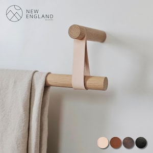 Puede incluir: Un toallero de madera con una correa de cuero. La barra est&aacute; montada en una pared blanca. El toallero est&aacute; hecho por New England Designs.