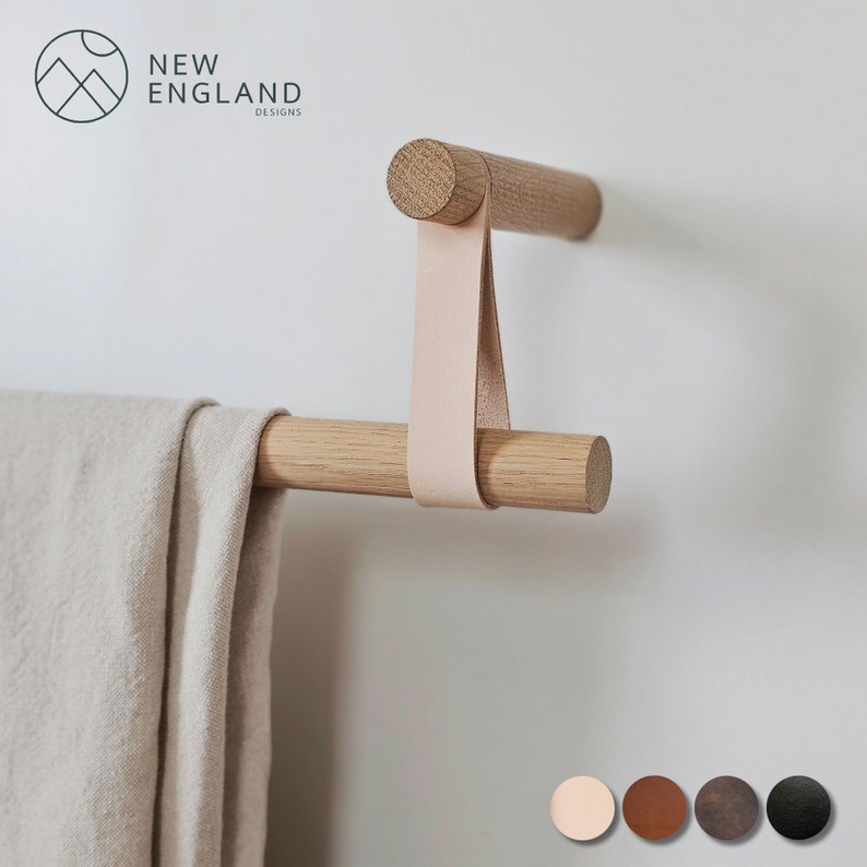Puede incluir: Un toallero de madera con una correa de cuero. La barra est&aacute; montada en una pared blanca. El toallero est&aacute; hecho por New England Designs.